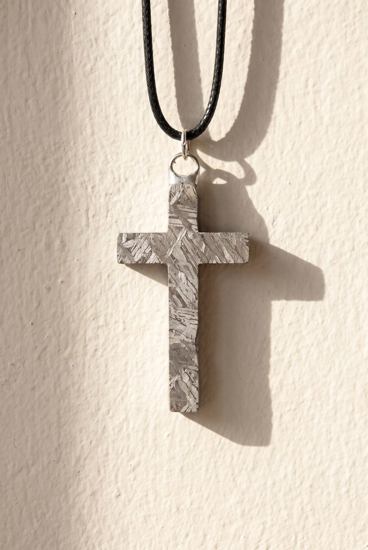 An Aletai meteorite cross pendant hanging against a plaster wall